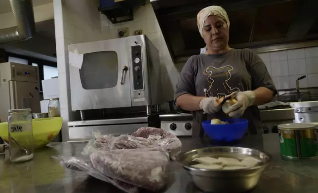 Ruqaia Agha, a Palestinian woman from Ramla, works in the HummusTown kitchen in Rome, Saturday, July 27, 2024. A pair of Syrians have created community that provides support to migrants and vulnerable people in Rome, by sharing the flavors of a homeland torn by civil war. Created in 2018 as a "humanitarian catering service," HummusTown originally aimed at raising funds for families and friends in Syria. (AP Photo/Gregorio Borgia)