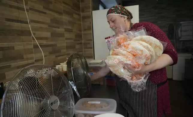 Jumana Farho, from Syria, holds slices of bread as she works in the HummusTown kitchen in Rome, Saturday, July 27, 2024. A pair of Syrians have created community that provides support to migrants and vulnerable people in Rome, by sharing the flavors of a homeland torn by civil war. Created in 2018 as a "humanitarian catering service," HummusTown originally aimed at raising funds for families and friends in Syria. (AP Photo/Gregorio Borgia)