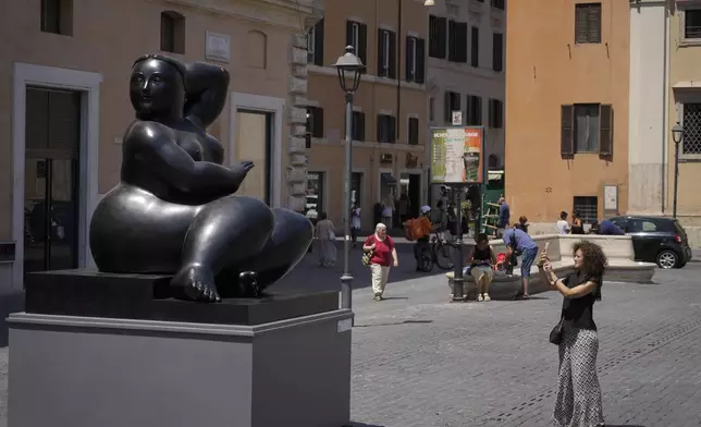 A woman take a picture at Botero's "Seated Woman" sculpture in Rome's Piazza San Silvestro, Friday, July 19, 2024. Rome's storied streets and piazzas have become a vibrant canvas for Fernando Botero's exuberant sculptures, turning the city into an open-air museum of voluminous forms and daring artistry. (AP Photo/Gregorio Borgia)