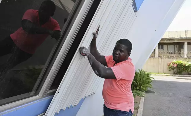 A man covers the windows of a building to protect it from the incoming Hurricane Beryl in Kingston, Jamaica, Tuesday, July 2, 2024. (AP Photo/Collin Reid)