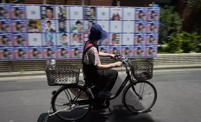 A woman bikes past an election campaign board installed for posters of Tokyo governor candidates in Tokyo, Sunday, July 7, 2024. Voters in Tokyo are casting ballots Sunday to decide whether to reelect conservative Yuriko Koike as governor of Japan's influential capital for a third four-year term. (AP Photo/Hiro Komae)