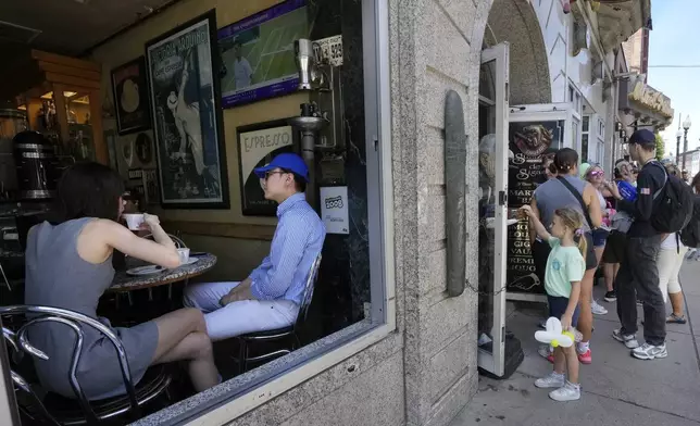 Bella Yu, left, and Xingwei Li, second from left, both of Boston, sit in a cafe as passers-by, right, make their way along a narrow street in Boston's historic North End neighborhood, Wednesday, July 3, 2024. A long Fourth of July holiday weekend in the United States is expected to create new travel records. Boston's North End neighborhood is a popular tourist destination. (AP Photo/Steven Senne)