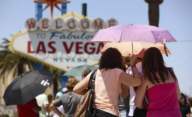 People use umbrellas to block the sun while waiting to take a photo at the "Welcome to Las Vegas" sign Monday, July 8, 2024, in Las Vegas. After causing deaths and shattering records in the West over the weekend, a long-running heat wave will again grip the U.S. on Monday, with hot temperatures also predicted for large parts of the East Coast and the South. (Wade Vandervort/Las Vegas Sun via AP)