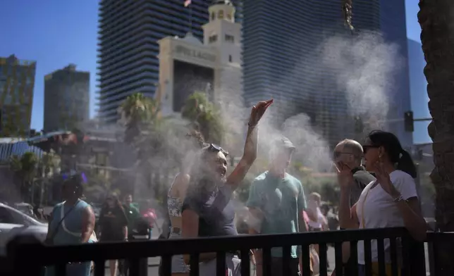 People cool off in misters along the Las Vegas Strip, Sunday, July 7, 2024, in Las Vegas. A heat wave is spreading across the Western U.S., the National Weather Service said, sending many residents in search of a cool haven from the dangerously high temperatures. (AP Photo/John Locher)