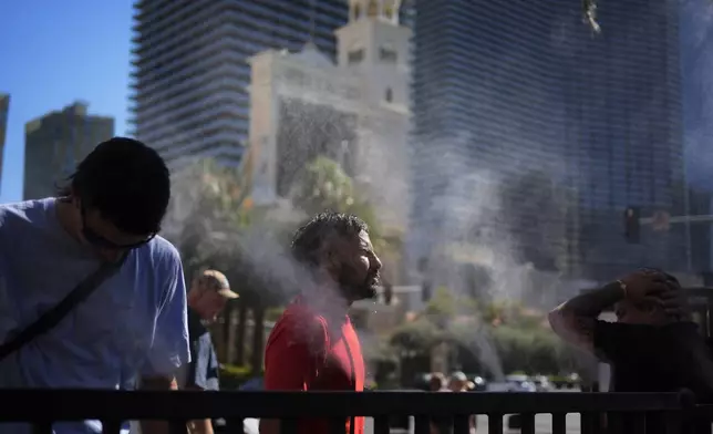 People cool off in misters along the Las Vegas Strip, Sunday, July 7, 2024, in Las Vegas. A heat wave is spreading across the Western U.S., the National Weather Service said, sending many residents in search of a cool haven from the dangerously high temperatures. (AP Photo/John Locher)