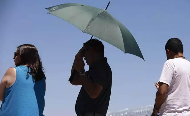 A person uses an umbrella to block the sun while waiting to take a photo at the "Welcome to Las Vegas" sign Monday, July 8, 2024, in Las Vegas. After causing deaths and shattering records in the West over the weekend, a long-running heat wave will again grip the U.S. on Monday, with hot temperatures also predicted for large parts of the East Coast and the South. (Wade Vandervort/Las Vegas Sun via AP)