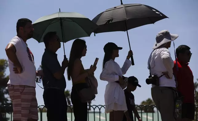 People use umbrellas to block the sun while waiting to take a photoat the "Welcome to Las Vegas" sign Monday, July 8, 2024, in Las Vegas. After causing deaths and shattering records in the West over the weekend, a long-running heat wave will again grip the U.S. on Monday, with hot temperatures also predicted for large parts of the East Coast and the South. (Wade Vandervort/Las Vegas Sun via AP)