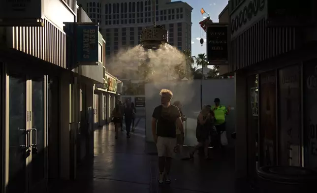 People walk through misters along the Las Vegas Strip, Sunday, July 7, 2024, in Las Vegas. The city set an all time record high of 120 F (48.8 C) Sunday as a heat wave spread across the Western U.S. sending many residents in search of a cool haven from the dangerously high temperatures. (AP Photo/John Locher)