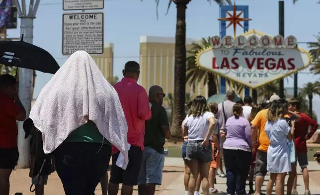 A person uses a blanket to block the sun while waiting to take a photo at the "Welcome to Las Vegas" sign Monday, July 8, 2024, in Las Vegas. After causing deaths and shattering records in the West over the weekend, a long-running heat wave will again grip the U.S. on Monday, with hot temperatures also predicted for large parts of the East Coast and the South. (Wade Vandervort/Las Vegas Sun via AP)