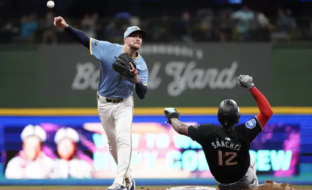 Milwaukee Brewers' Brice Turang, left, turns a double play after tagging out Miami Marlins' Jesús Sánchez (12) at second base during the fifth inning of a baseball game Friday, July 26, 2024, in Milwaukee. (AP Photo/Aaron Gash)