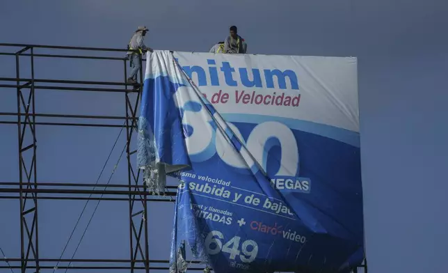 Workers remove an advertisement from a billboard for protection ahead of Hurricane Beryl's expected arrival, in Playa del Carmen, Mexico, Wednesday, July 3, 2024. (AP Photo/Fernando Llano)