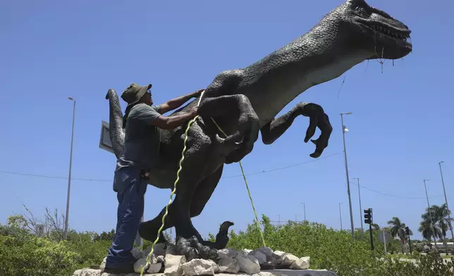A worker secures a dinosaur statue at a theme park ahead of Hurricane Beryl's expected arrival in Chicxulub, Mexico, Thursday, July 4, 2024. (AP Photo/Martin Zetina)