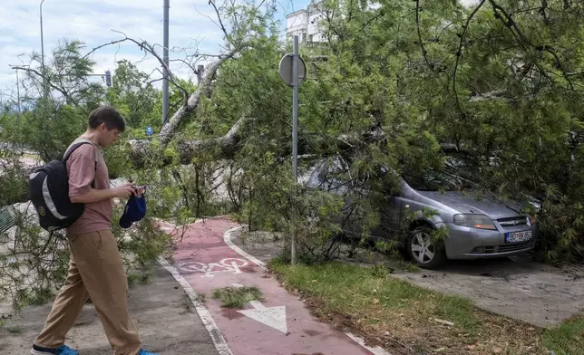 A person walks past a downed tree after a powerful storm in Montenegro's capital Podgorica, Tuesday, July 2, 2024. A powerful storm has swept through countries in the western Balkans after several days of sizzling temperatures, killing two people and damaging houses, pulling out trees and flooding streets, officials said on Tuesday. (AP Photo/Risto Bozovic)