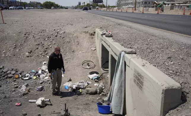 Mark Paulson, a Public Response and Code Enforcement officer, holds cans of cold water while checking on a homeless encampment, Wednesday, July 10, 2024, in Henderson, Nev. About 14 officers from the Office of Public Response drove around the city Wednesday offering water, electrolytes, free bus tickets and rides to cooling centers during a heat emergency. (AP Photo/John Locher)