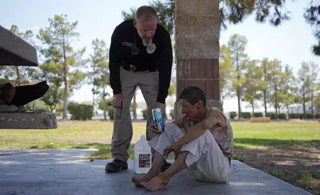 Mark Paulson, a Public Response and Code Enforcement officer, checks on Deb Billet, 66, before calling an ambulance to take her to a hospital for heat-related symptoms Wednesday, July 10, 2024, in Henderson, Nev. Billet has been living on the street. About 14 officers from the Office of Public Response drove around the city Wednesday offering water, electrolytes, free bus tickets and rides to cooling centers during a heat emergency. (AP Photo/John Locher)