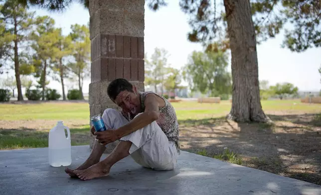 Deb Billet, 66, rests on the ground while drinking cold water given to her by Henderson Public Response officers before they called an ambulance to take her to hospital for heat-related symptoms Wednesday, July 10, 2024, in Henderson, Nev. Billet has been living on the street. About 14 officers from the Office of Public Response in Henderson drove around the city Wednesday, offering water, electrolytes, free bus tickets, and rides to cooling centers during a heat emergency. (AP Photo/John Locher)