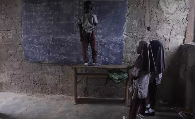 Students of Excellent Moral School attempt to answer a mathematics question on a blackboard inside a dimly lit classroom in Ibadan, Nigeria, Tuesday, May 28, 2024. The lack of reliable electricity severely affects education and businesses in Nigeria. (AP Photo/Sunday Alamba)