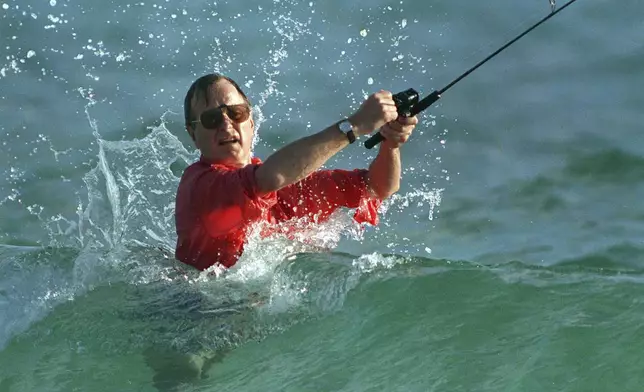 FILE - Waves splash President-elect George Bush as he casts a line while surf-fishing in Gulf Stream, Fla., Nov. 12, 1988, shortly after winning the 1988 Presidential election. (AP Photo/Kathy Willens, File)