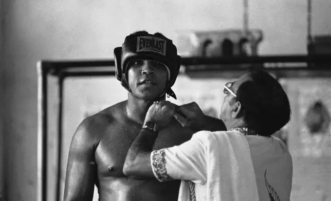 FILE - World heavyweight champion Muhammad Ali has his head gear adjusted by Chris Dundee, boxing trainer from the well-known Fifth Street Gym in Miami Beach, Fla., on Dec. 21, 1977. (AP Photo/Kathy Willens, File)