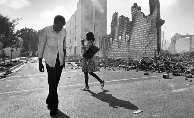 FILE - People walk past ruins in the Culmer section of Miami on May 19, 1980, after rioting over the acquittal of four police officers charged with the 1979 beating death of Arthur McDuffie, a black motorcyclist. (AP Photo/Kathy Willens, File)