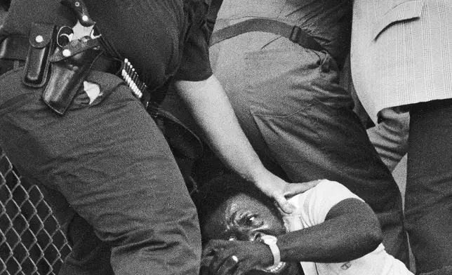 FILE - A Border Patrol officer clubs a Haitian refugee who broke through gates of Krome Detention Center, in Miami, 1981. (AP Photo/ Kathy Willens, File)