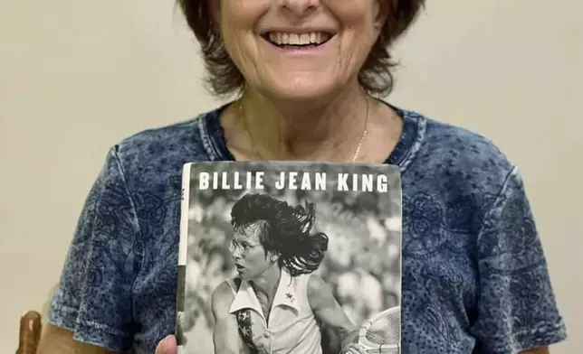 In this 2021 photo provided by the Willens family, Kathy Willens poses for a photo with a copy of Billie Jean King's autobiography "All In" with an image Willens took of King in 1977 on the cover. (Willens family via AP)