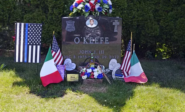 FILE - Flags, flowers and remembrances flank the headstone of John O'Keefe, a Boston police officer, at Blue Hill Cemetery, Thursday, June 27, 2024, in Braintree, Mass. A judge declared a mistrial Monday, July 1, 2024, after jurors deadlocked in the case of Karen Read, who was accused of killing her police officer boyfriend, O'Keefe, by striking him with her SUV and leaving him in a snowstorm. Prosecutors said in a statement that they intend to retry the case. (AP Photo/Charles Krupa, File)