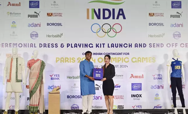 This image shared by the Public Information Bureau shows Dr. Mansukh Mandaviya, Indian Minister of Youth Affairs and Sports, left, presenting a kit to former Indian Olympian, Mary Kom, as mannequins display India's ceremonial and playing kits for the Paris Olympics in New Delhi, India, Sunday, June 30, 2024. (Press Information Bureau via AP)