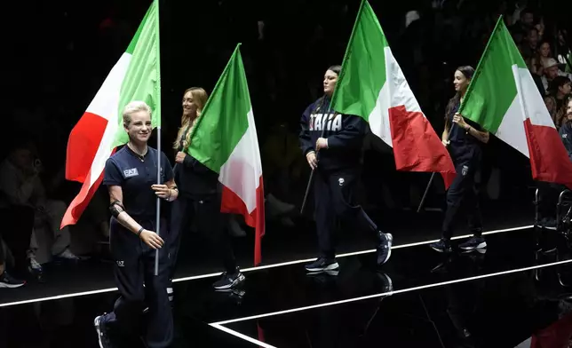 FILE - Paralympic champion Beatrice 'Bebe' Vio, left, wears with her teammates a creation as part of the Emporio Armani men's Spring Summer 2024 collection as they hold a Italian flag, presented in Milan, Italy, Saturday, June 17, 2023. Italian athletes will be elegantly attired in Emporio Armani uniforms, as they have for every Olympics since 2012. (AP Photo/Luca Bruno, File)