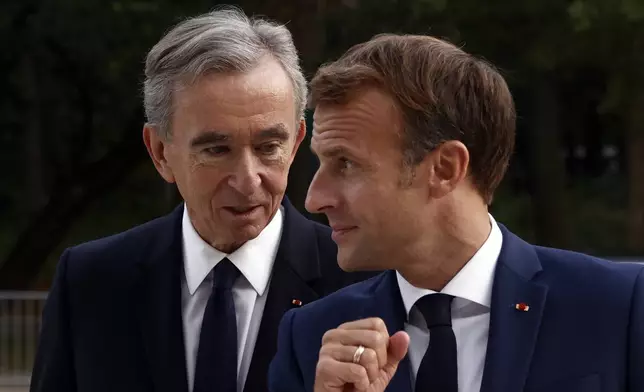 FILE - LVMH luxury group CEO Bernard Arnault, left, and French President Emmanuel Macron arrive at Fondation Louis Vuitton to visit the exhibition 'The Morozov Collection, Icons of Modern Art' in Paris, Tuesday, Sept. 21, 2021. With a major sponsorship role aimed at burnishing the image of the Paris 2024 Summer Olympic Games and the French capital, it's a new chapter in LVMH's specialty of selling exclusivity at a grand scale under its chair and CEO, Arnault. (Yoan Valat/Pool Photo via AP, File)