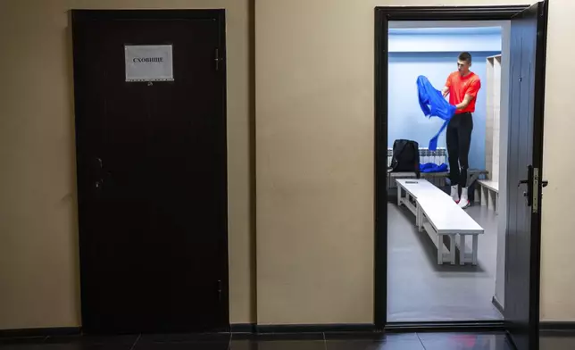 High jumper Oleh Doroshchuk changes his clothes in a dressing room with a sign that reads in Ukrainian, "Shelter," prior a training session at regional youth sport school for the Olympics, in Kropyvnytskyi, Ukraine, Thursday, April 18, 2024. Doroshchuk says he’s been forced to look inside himself, questioning whether it’s morally right that he’s “just training” when other men are defending front lines. (AP Photo/Francisco Seco)