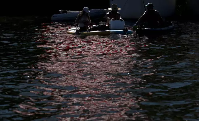 With an American flag reflected in the Willamette River, people sit on their paddle boards and listen to the music at the Waterfront Blues Festival on Friday, July 5, 2024, in Portland, Ore. A slow-moving and potentially record-setting heat wave is spreading across the Western U.S., sending many residents in search of a cool haven from the dangerously high temperatures. (AP Photo/Jenny Kane)