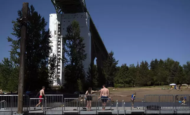 People walk on the dock at Cathedral City Park on Friday, July 5, 2024, in Portland, Ore. A slow-moving and potentially record-setting heat wave is spreading across the Western U.S., sending many residents in search of a cool haven from the dangerously high temperatures. (AP Photo/Jenny Kane)