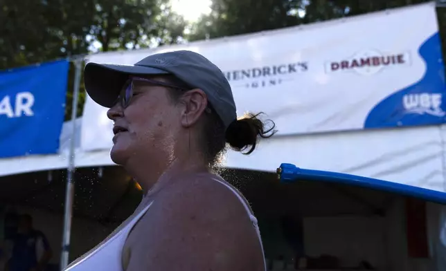 Gina Rowlett uses the mister to cool off at the Waterfront Blues Festival on Friday, July 5, 2024, in Portland, Ore. A slow-moving and potentially record-setting heat wave is spreading across the Western U.S., sending many residents in search of a cool haven from the dangerously high temperatures. (AP Photo/Jenny Kane)