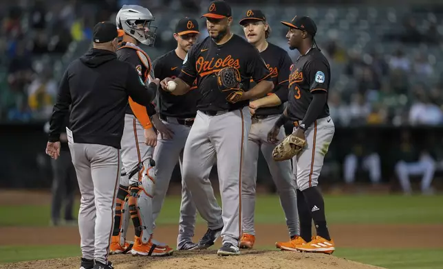 Baltimore Orioles pitcher Albert Suárez, center, hands the ball over to manager Brandon Hyde, left, as he exits during the seventh inning of a baseball game against the Oakland Athletics, Friday, July 5, 2024, in Oakland, Calif. (AP Photo/Godofredo A. Vásquez)