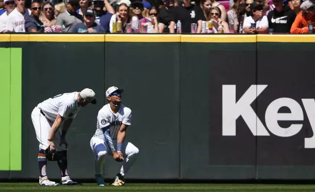 Seattle Mariners left fielder Luke Raley, left, checks on center fielder Julio Rodríguez, right, holds his wrist after falling while catching a fly ball hit by Baltimore Orioles' Jordan Westburg during the sixth inning of a baseball game Thursday, July 4, 2024, in Seattle. (AP Photo/Lindsey Wasson)