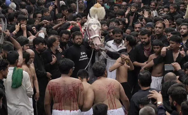 Shiite Muslims flagellate themselves with knifes attached to chains in front of a horse, that symbolizes the horse that carried Imam Hussein during the battle of Karbala, during a Muharram procession, in Lahore, Pakistan, Tuesday, July 16, 2024. Muharram, the first month of the Islamic calendar, is a month of mourning for Shiites in remembrance of the death of Hussein, the grandson of the Prophet Muhammad, at the Battle of Karbala in present-day Iraq in the 7th century. (AP Photo/K.M. Chaudary)