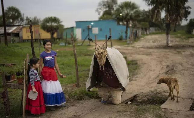 Sofia Maldonado, wearing a skirt in national colors, stands next to her father dressed as "Toro Kandil" for the San Juan festivities, in the Kuna Pyapy Mbarete neighborhood, on the outskirts of Asuncion, Paraguay, Saturday, July 6, 2024. The heads of state from South America's Mercosur trade bloc will gather in Asuncion on July 8. (AP Photo/Rodrigo Abd)