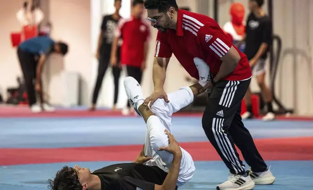 Palestinian Omar Yaser Ismail stretches with coach Humaid Almheiri during his Taekwondo training session at the Sharjah Sports Club in Sharjah, United Arab Emirates, Thursday, June 20, 2024. (AP Photo/Martin Dokoupil)