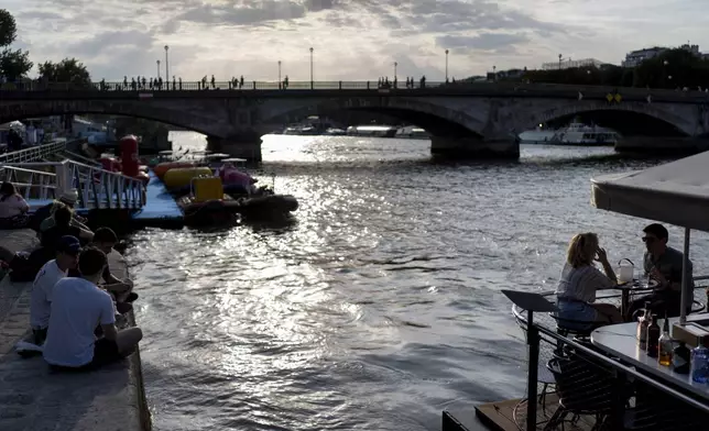 People sit out along the Seine river during the 2024 Summer Olympics, Monday, July 29, 2024, in Paris. As the Olympics continue in Paris, the Seine River's water quality remains a major area of concern for officials. Organizers of the triathlon event cancelled swimming practice on Monday for the second day in a row because of poor water quality. Event organizers hope sunny weather will make swimming viable on Tuesday when the triathlon begins. (AP Photo/David Goldman)