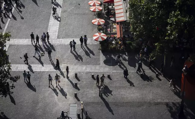 The setting sun casts shadows of pedestrians passing a cafe outside the George Pompidou Beaubourg museum ahead of the 2024 Summer Olympics, Sunday, July 21, 2024, in Paris. (AP Photo/David Goldman)