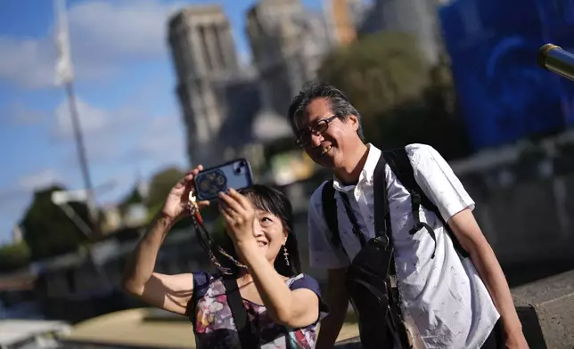 Japanese tourists Ken Kito and his wife snap a selfie with the under-construction Notre-Dame Cathedral in the background, ahead of the 2024 Summer Olympics, Monday, July 22, 2024, in Paris, France. (AP Photo/Rebecca Blackwell)