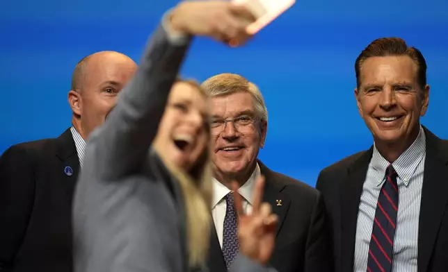 A woman makes a selfie with Utah Gov. Spencer Cox, left, and IOC president Thomas Bach, center, during the 142nd IOC session at the 2024 Summer Olympics, Wednesday, July 24, 2024, in Paris, France, after Salt Lake City was confirmed as host for the 2034 Winter Games by International Olympic Committee. (AP Photo/Natacha Pisarenko)