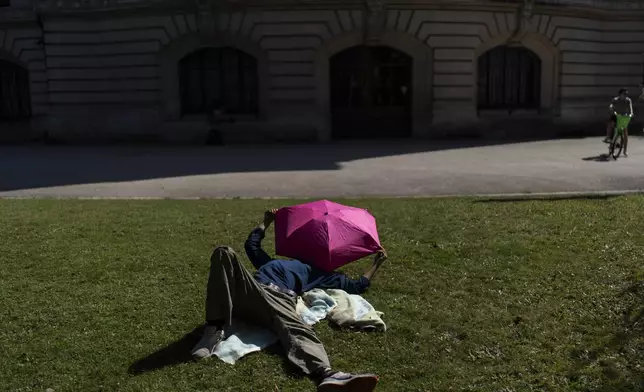 A man uses an umbrella to shield himself from the hot afternoon sun near the Grand Palais fencing venue at the 2024 Summer Olympics, Monday, July 29, 2024, in Paris. (AP Photo/David Goldman)