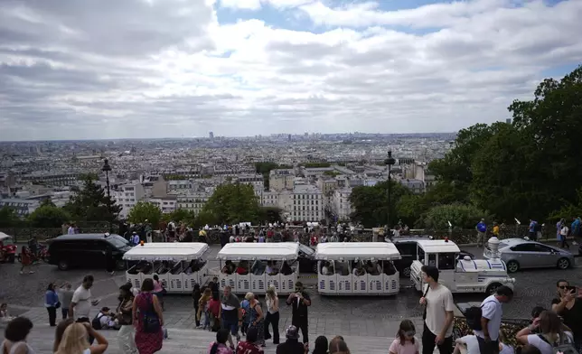 A tourist train passes as people visit the steps below Sacre Coeur of Montmartre Basilica, ahead of the 2024 Summer Olympics, Monday, July 22, 2024, in Paris, France. (AP Photo/Rebecca Blackwell)