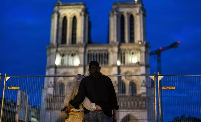 A couple stand next to a security fence placed around Notre Dame cathedral ahead of the 2024 Summer Olympics, Monday, July 22, 2024, in Paris. (AP Photo/Francisco Seco)