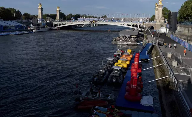 Watercraft and buoys sit along the Seine river as the triathlon event venue on the Pont Alexandre III bridge stands in the background at the 2024 Summer Olympics, Sunday, July 28, 2024, in Paris. (AP Photo/David Goldman)