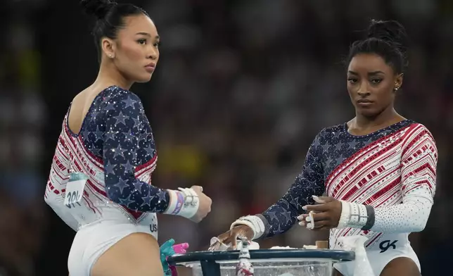 Simone Biles, and Suni Lee, left, of the United States, prepare to performs on the uneven bars during the women's artistic gymnastics team finals round at Bercy Arena at the 2024 Summer Olympics, Tuesday, July 30, 2024, in Paris, France. (AP Photo/Charlie Riedel)