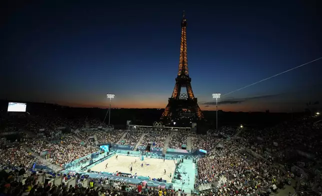 The Eiffel Tower sparkles at dusk as the United States, on left, plays Czechia in a beach volleyball match at the 2024 Summer Olympics, Sunday, July 28, 2024, in Paris, France. (AP Photo/Robert F. Bukaty)