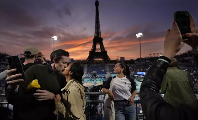 Maeva Ratoanina and Pierre-Yves Massive, of Paris, enjoy a romantic moment while taking selfies during sunset at Eiffel Tower Stadium prior to a beach volleyball match between The United States and Canada at the 2024 Summer Olympics, Saturday, July 27, 2024, in Paris, France. (AP Photo/Robert F. Bukaty)